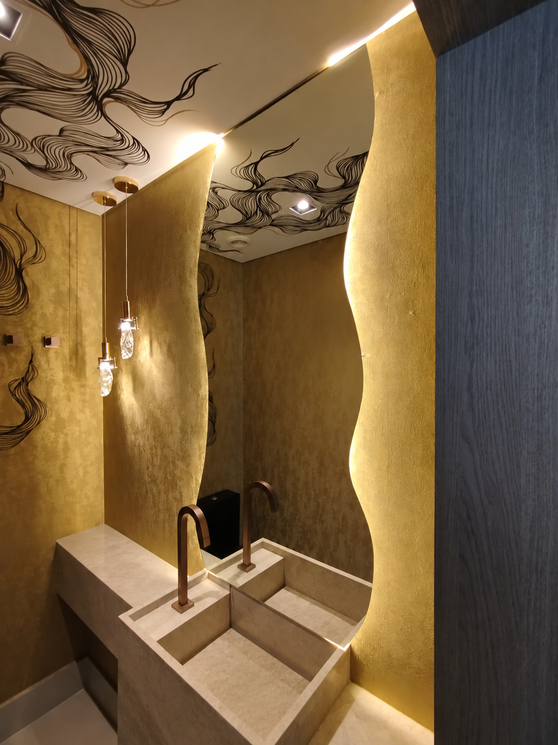Espelho orgânico com iluminação integrada em lavabo com revestimento dourado.